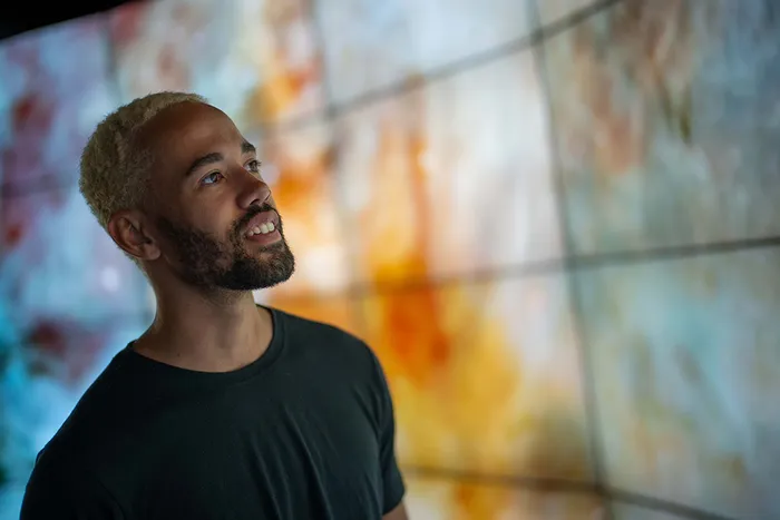 Man with short blonde hair and beard gazes thoughtfully at a large, colorful abstract display.