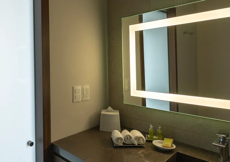 Residential living room at night with a grey sofa, wall-mounted television and warm ambient light — Simon 26 iO scene with smart control through Alexa and Google Home.