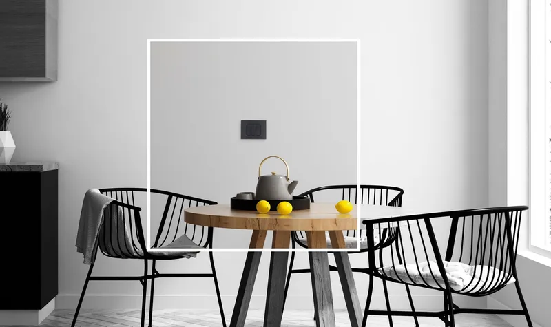 Comedor en blanco y negro con mesa redonda, sillas metálicas y mecanismo Simon 82 Prisma instalado en la pared