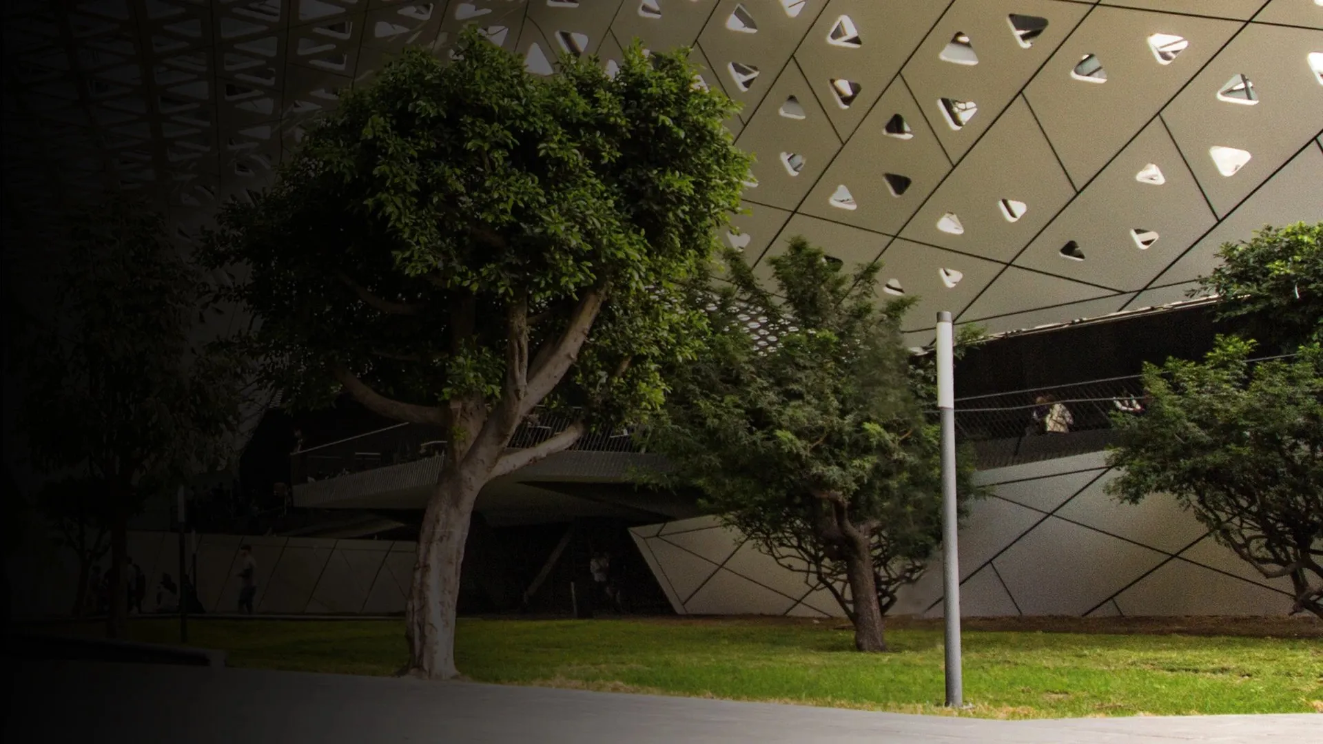 Simon Enif illuminating a nocturnal architectural façade with trees and a vertical luminaire in the foreground.