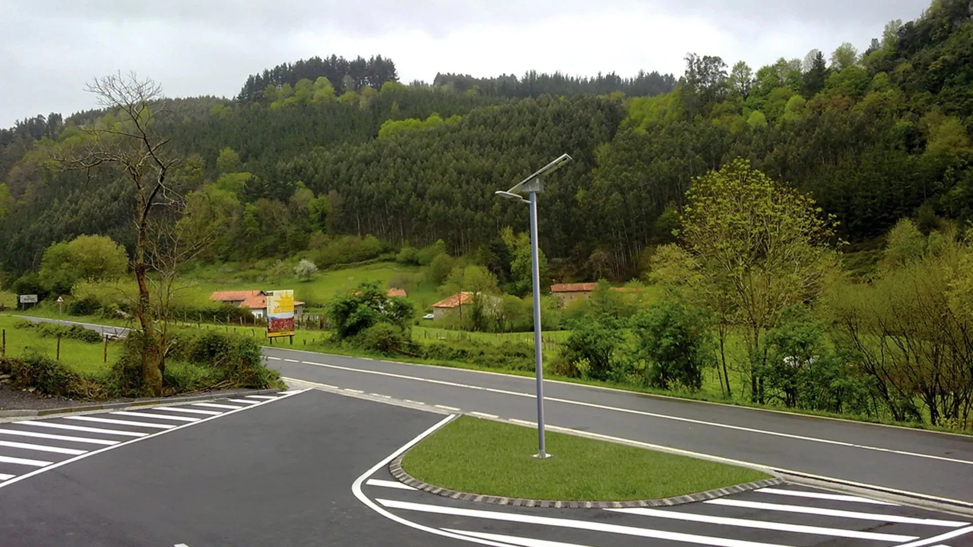 Simon Magnolia instalada en una carretera rural de doble carril rodeada de bosques verdes — luminaria fotovoltaica autónoma sobre poste de acero.