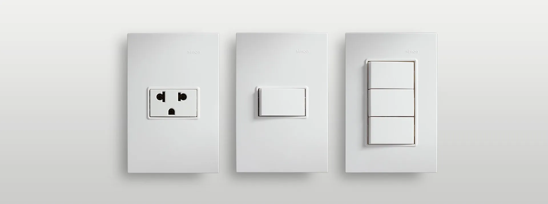 Three Simon 23 plates on a white wall — 2P+T socket outlet, 1-key switch and 3-switch plate