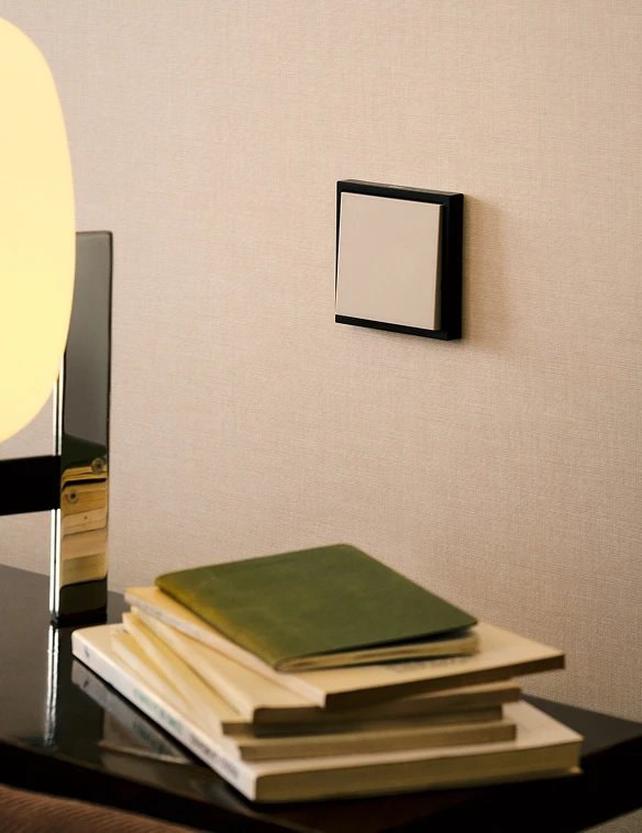 Mécanisme Simon 360 Combinaison S36 (bicolore) sur un mur crème avec lampe de table dorée et pile de livres