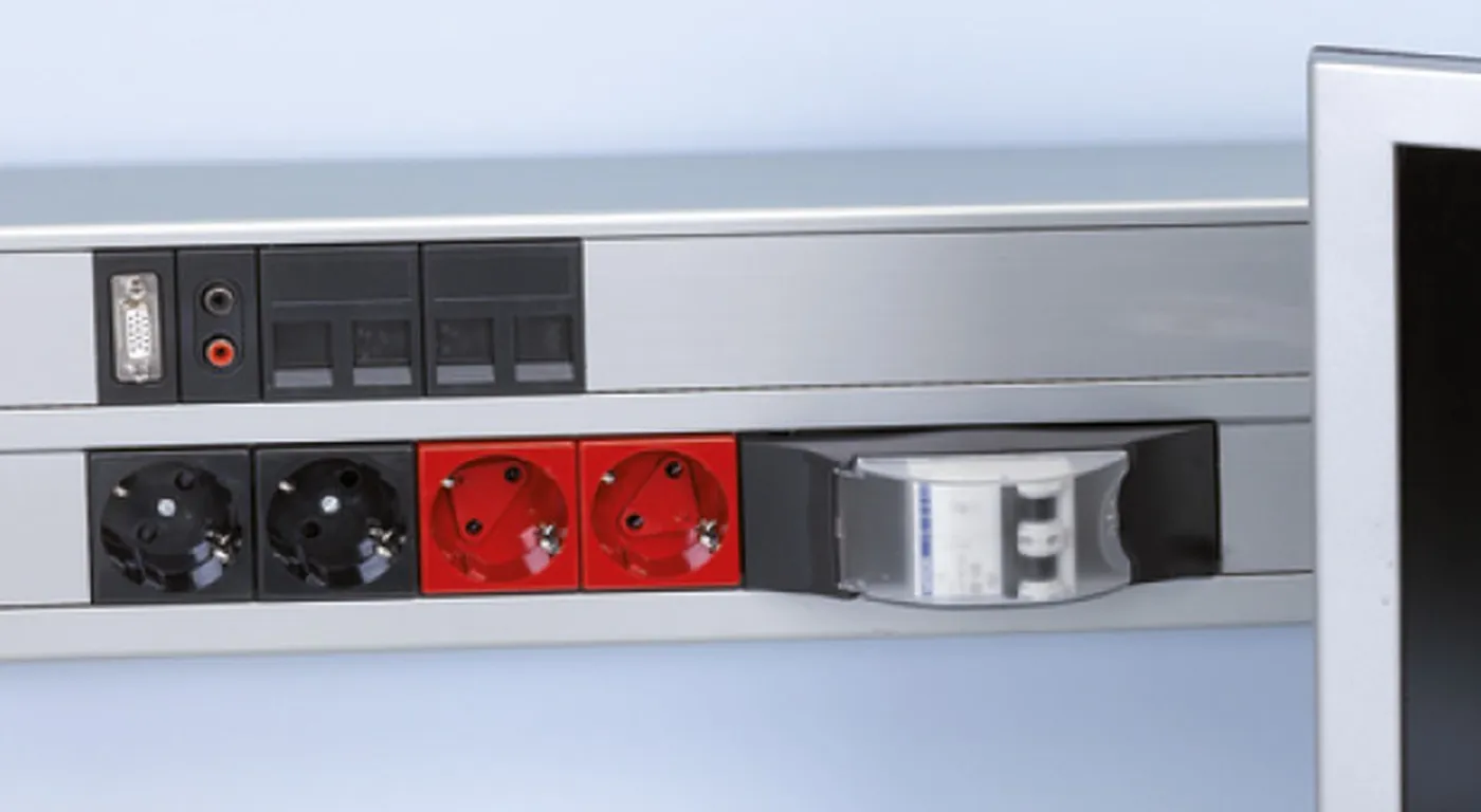 Canal K45 de aluminio anodizado con bases de enchufe y conectores junto al monitor