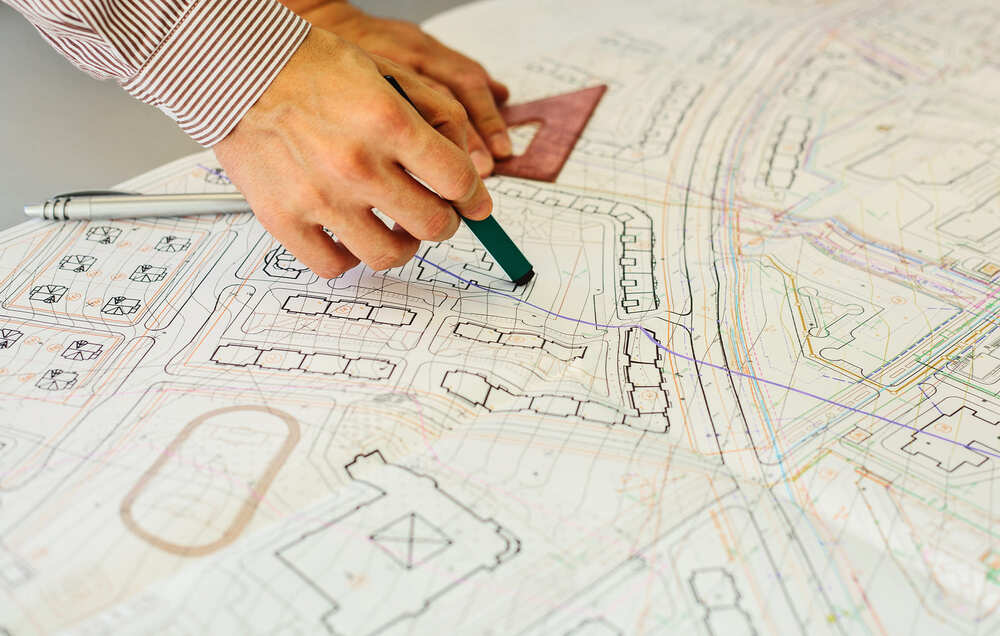 una mano de arquitecto hace trazos sobre un plano urbano