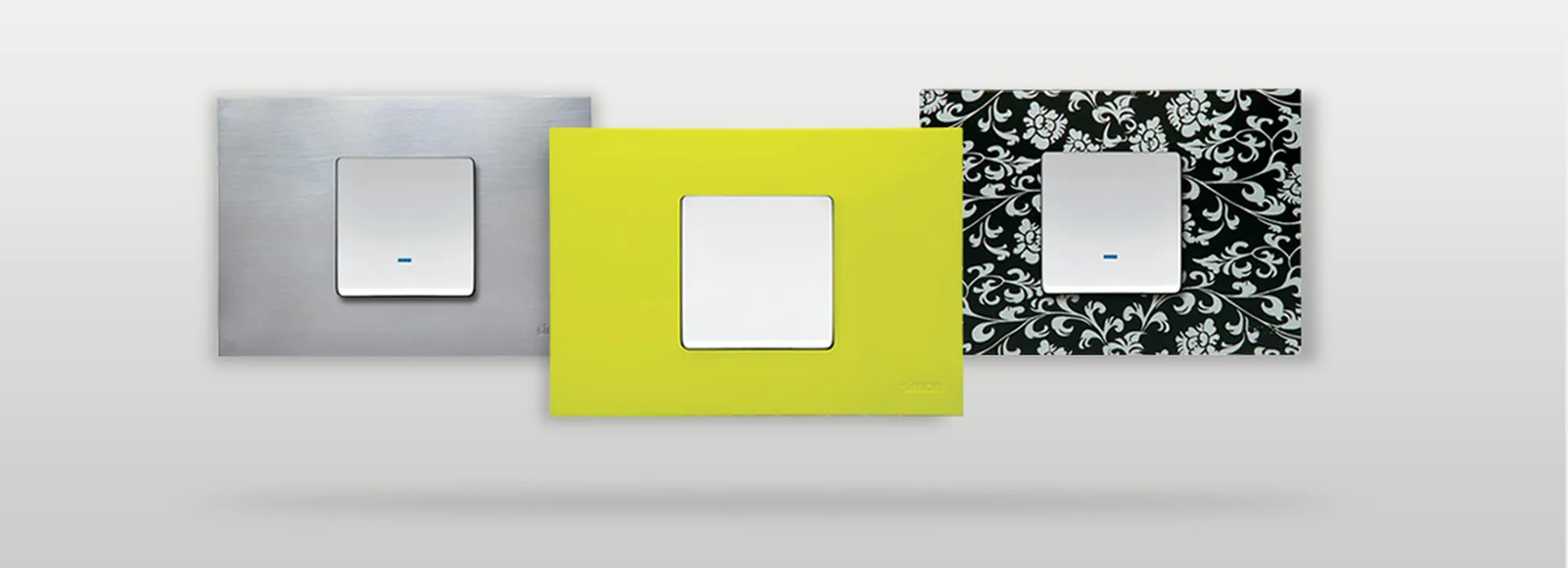 Simon 27 Play — tres placas alineadas sobre fondo gris mostrando distintos acabados (blanco, naranja, transparente).