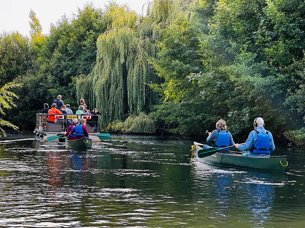 The audience are wearing headphones paddling canoes down the River To