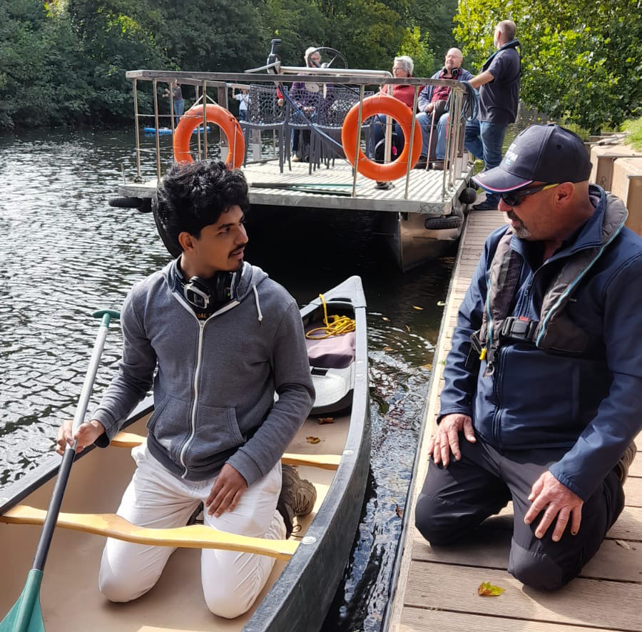 A young audience member kneeling in a canoe while listening to the safety briefing from boat skipper Ryan