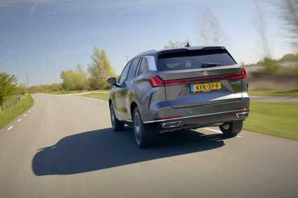 A gray MGS9 drives on a sunny, tree-lined rural road, showcasing sleek design and European license plate.