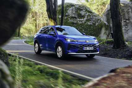 Blue SUV driving on a forest road. Moss-covered rocks and trees surround the path, creating a serene, natural atmosphere.