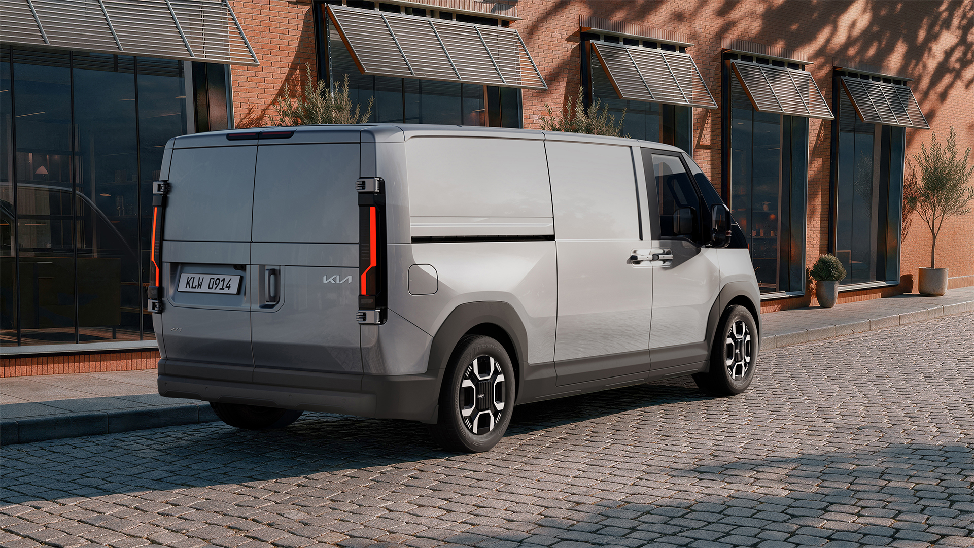 Silver van parked on a cobblestone street beside a brick building with large windows and plants.