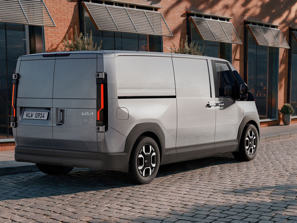 Silver van parked on a cobblestone street beside a brick building with large windows and plants.