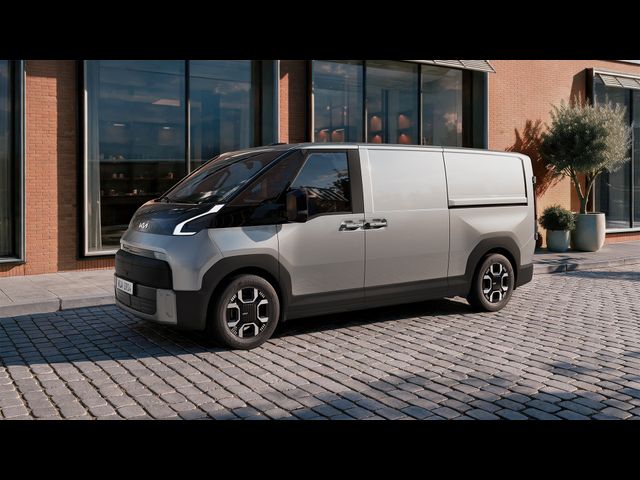 A modern, silver van parked on a cobblestone street in front of a building with large windows and greenery.