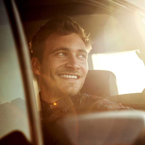 Man smiling while sitting in a car, bathed in warm sunlight streaming through the window.