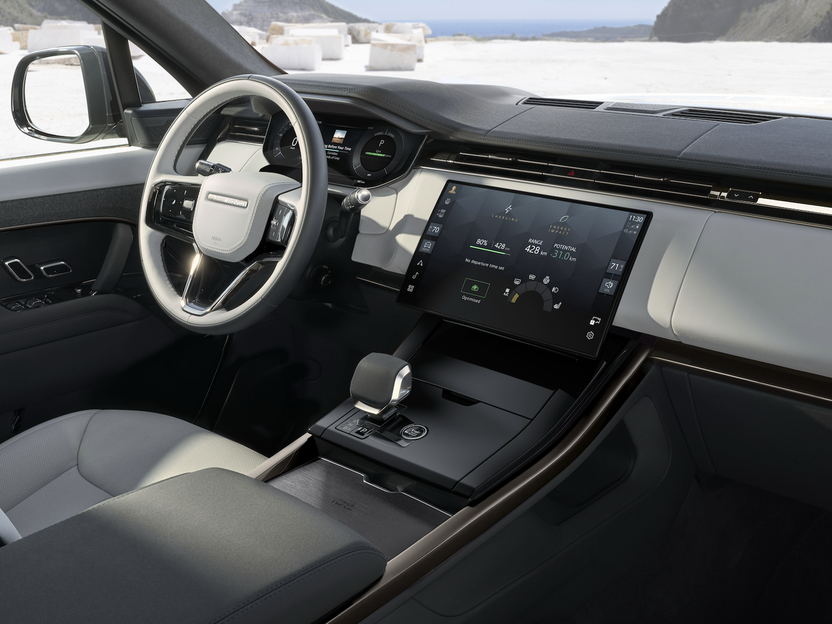 Luxury car interior with a sleek steering wheel, modern dashboard screens, and a panoramic view of a rugged, snowy landscape through the window.