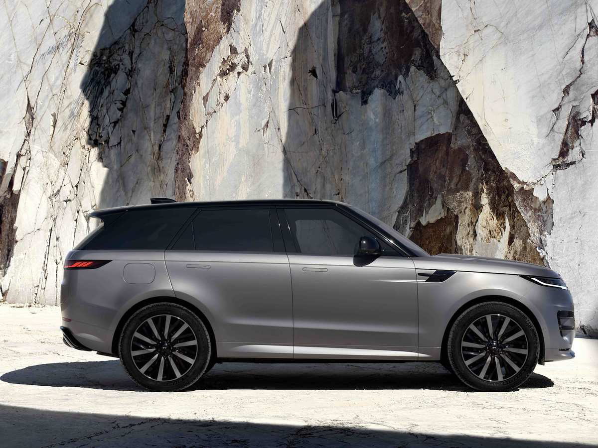 Silver SUV parked beside a textured rock wall, casting shadows in a sunlit quarry-like setting.