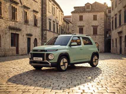 Green Hyundai Inster Lounge parked on cobblestone street in a European-style stone building square at sunset.