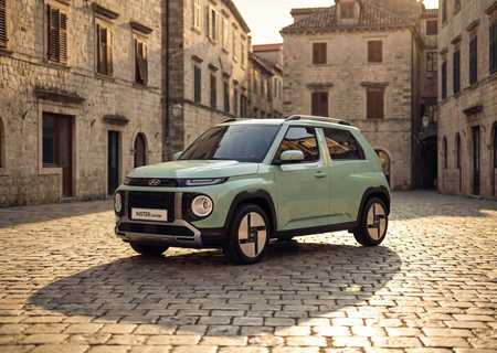 Green Hyundai Inster Lounge parked on cobblestone street in a European-style stone building square at sunset.