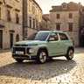 Green Hyundai Inster Lounge parked on cobblestone street in a European-style stone building square at sunset.