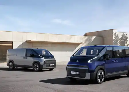 Two modern vans, one silver and one blue, parked outside a beige building on a clear day.