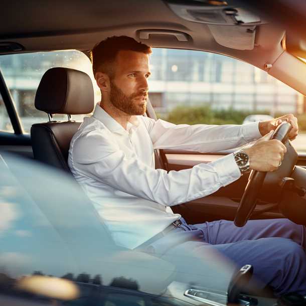 Man in a white shirt driving a car, with sunlight streaming through the window, creating a warm glow inside the vehicle.