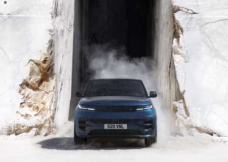 A blue Range Rover emerges from a marble quarry, surrounded by dust and stone walls.