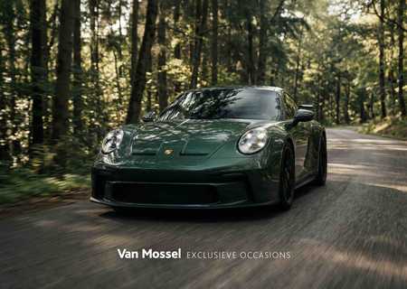Green sports car driving through a forested road in daylight, surrounded by lush trees. Van Mossel logo displayed at the bottom.