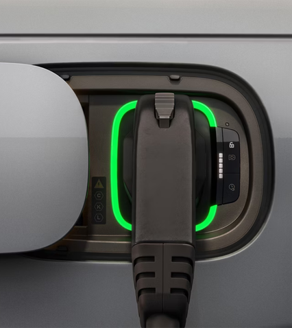 Electric vehicle charging port with plug inserted, surrounded by a green light indicator, on a silver surface.