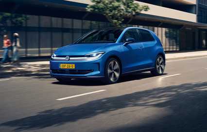 Blue Volkswagen hatchback driving on a city street, with blurred background and buildings.