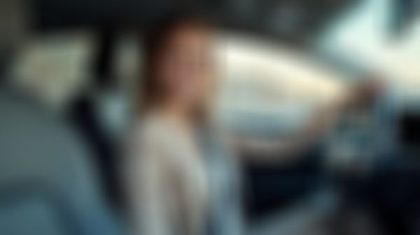 Frau im Business Outfit sitzt im Auto und lächelt in die Kamera