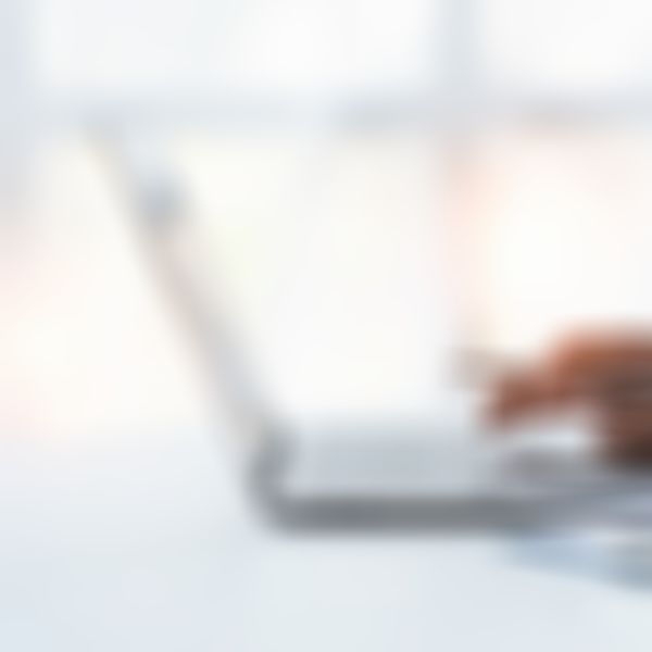 Männliches Hand mit Kugelschreiber in der Hand tippt auf Laptop.