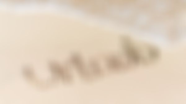 Schriftzug URLAUB in den Sand geschrieben und eine Welle Meerwasser fließt darauf zu