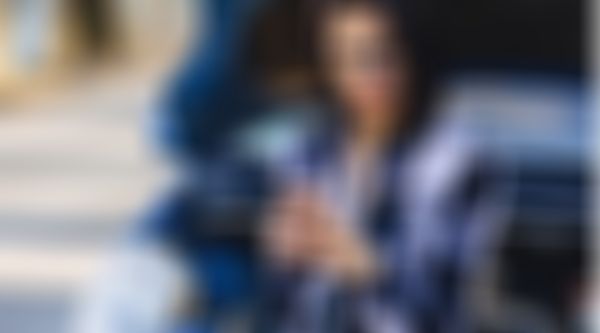 Junge Frau sitzt vor offener Motorhaube und schaut ins Handy.