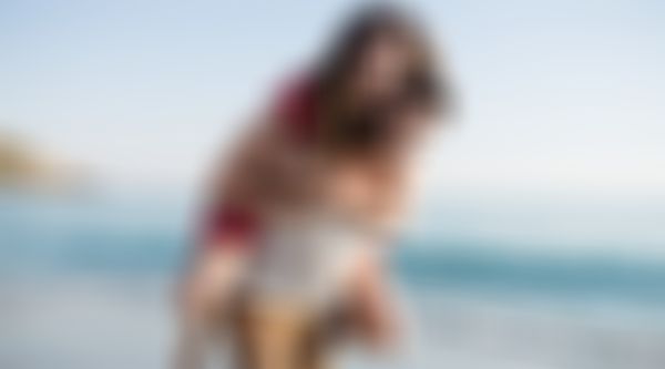 Mann trägt Frau auf dem Rücken den Strand entlang