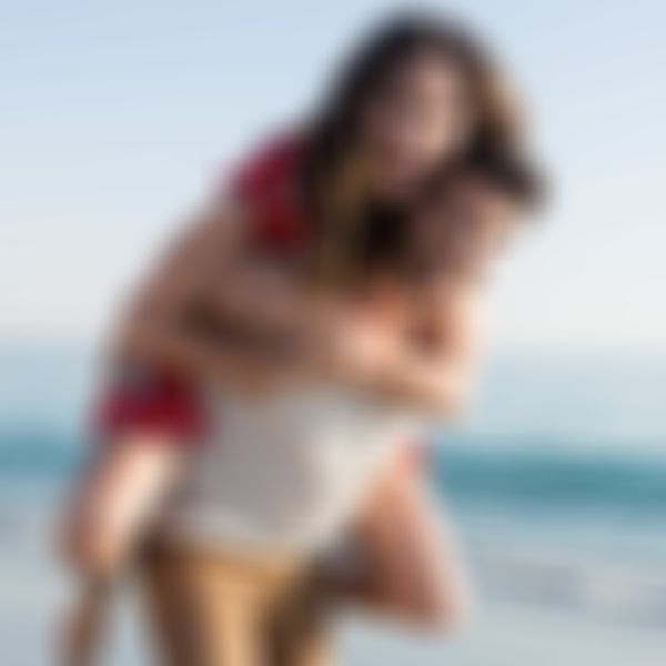 Mann trägt Frau auf dem Rücken den Strand entlang