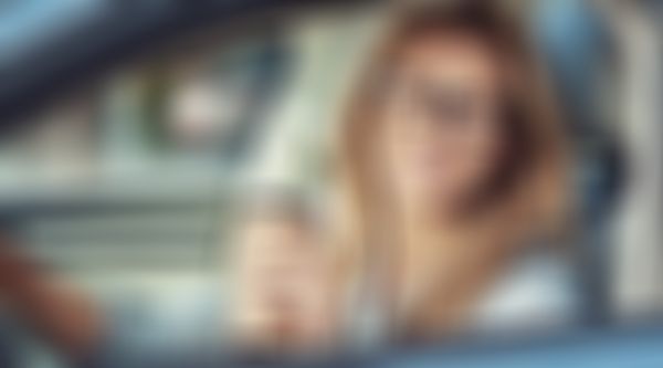 Kfz-Haftpflicht-Versicherung - Frau im Auto bei offenem Fenster und einem Kaffee in der Hand