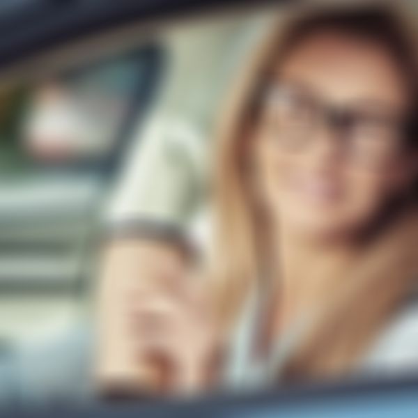 Kfz-Haftpflicht-Versicherung - Frau im Auto bei offenem Fenster und einem Kaffee in der Hand