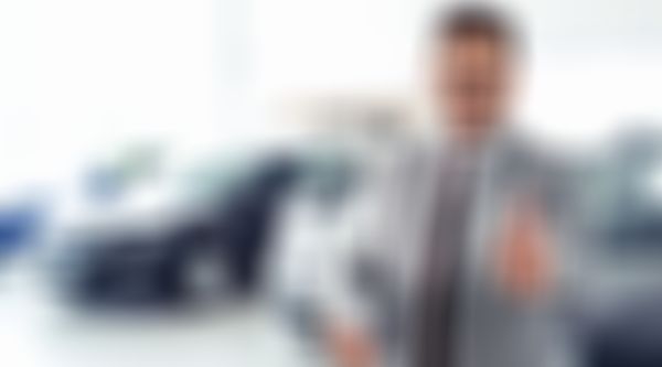 Autohausverkäufer lächelt und zeigt den Daumen nach oben.