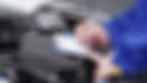 Kfz Mechaniker steht bei offener Motorhaube und füllt Prüfbericht aus