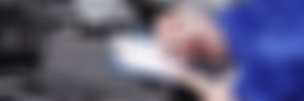 Kfz Mechaniker steht bei offener Motorhaube und füllt Prüfbericht aus