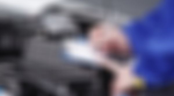 Kfz Mechaniker steht bei offener Motorhaube und füllt Prüfbericht aus