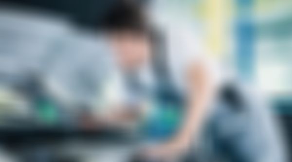 Mechaniker lehnt sich mit Taschenlampe über die Motorhaube