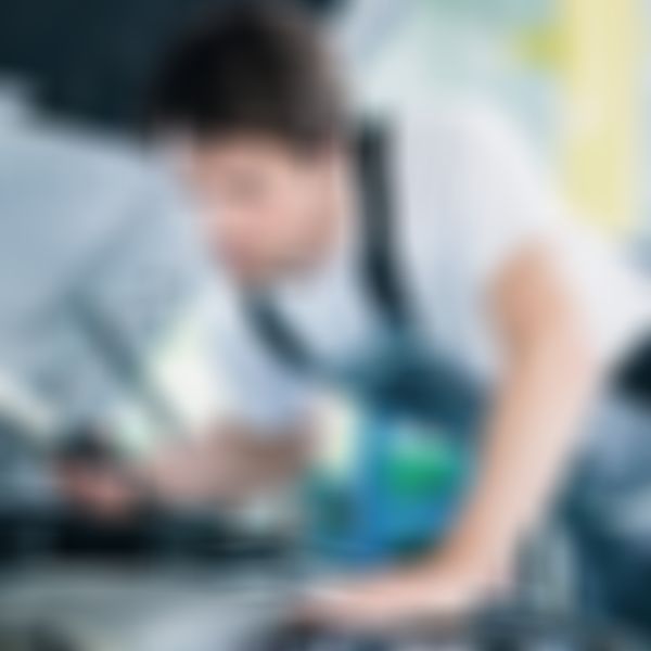 Mechaniker lehnt sich mit Taschenlampe über die Motorhaube