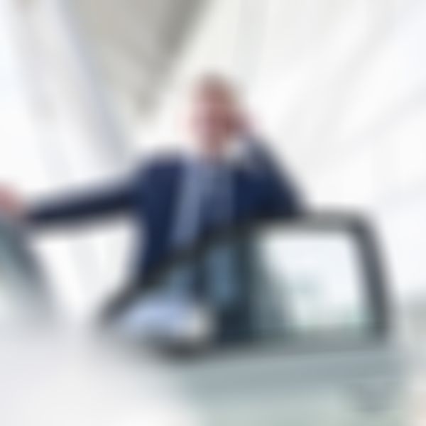 Mann im Anzug steht bei der offenen Autotür und telefoniert