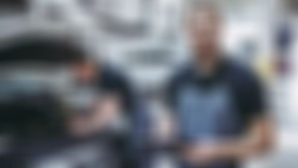 Mechaniker steht in Werkstatt vor Auto mit offener Motorhaube.