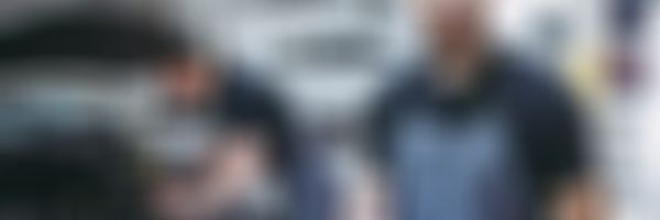 Mechaniker steht in Werkstatt vor Auto mit offener Motorhaube.