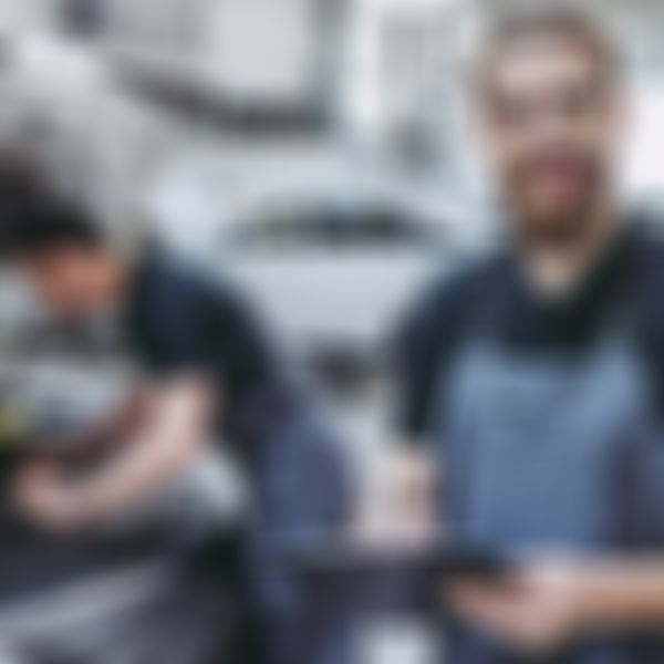 Mechaniker steht in Werkstatt vor Auto mit offener Motorhaube.