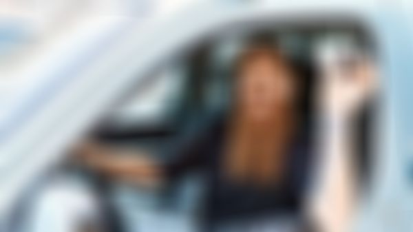 Lächelnder junger Mann sitzt bei offenem Fenster im Auto und hält Autoschlüssel in der Hand.