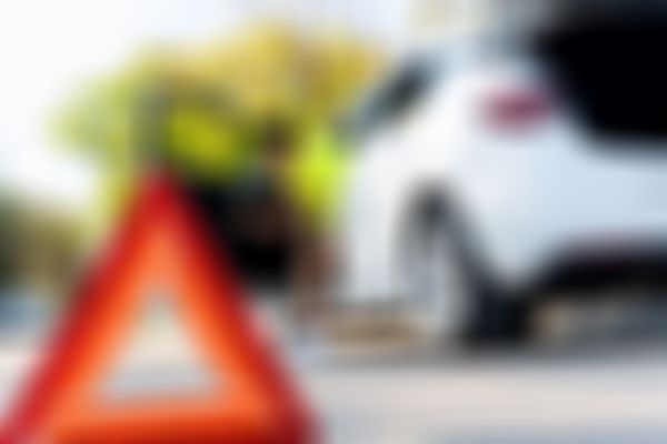 Warndreieck im Vordergrund, Frau steigt im Hintergrund aus weißem Auto aus