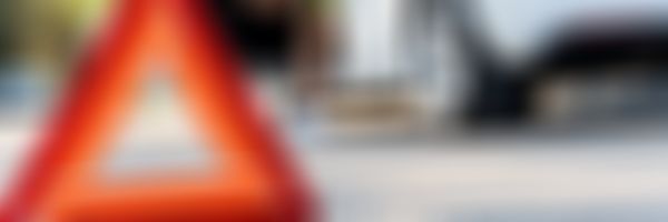 Warndreieck im Vordergrund, Frau steigt im Hintergrund aus weißem Auto aus